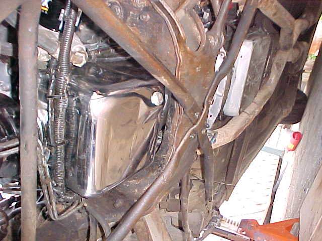 Chrome tank mounted among rusty frame tubes and wiring under a vehicle