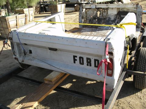 1966 Ford Bronco - The rear of a white Ford pickup truck bed is secured to a trailer for transport.