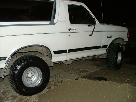 1988 Ford Bronco - Side profile of a white 1988 Ford Bronco, equipped with large off-road tires.