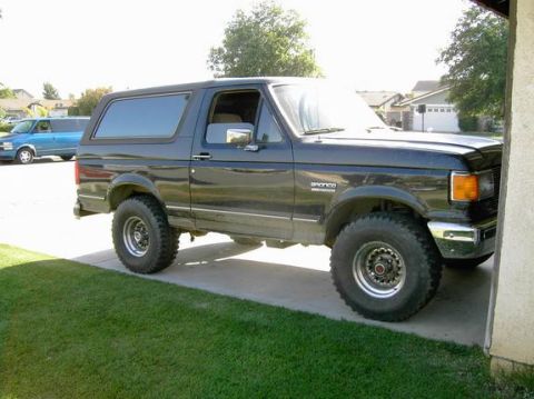 1988 Ford Bronco - This black 1988 Ford Bronco is parked on a driveway next to a house.