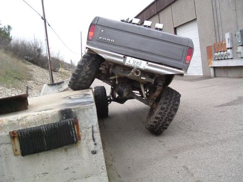 1979 Ford Bronco - Modified Ford pickup truck with large tires navigating a concrete obstacle. License plate 324SE is visible.