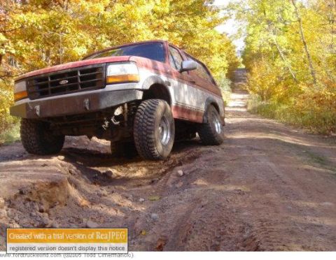 1991 Ford Bronco - This Ford Bronco is navigating a rough, rutted dirt path surrounded by autumn trees.