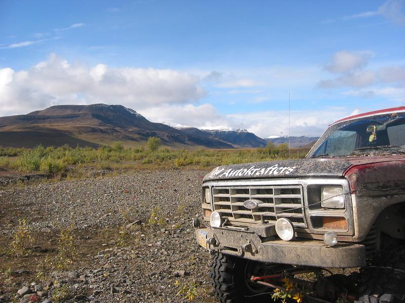 Muddy red Ford Bronco front-left view on gravel with mountains behind