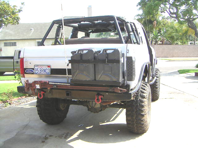 Rear of white Ford Bronco with roll cage, off-road bumper, jerry cans and big tires on driveway