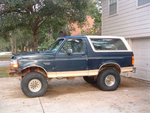 1993 Ford Bronco - Side view of a dark blue 1993 Ford Bronco with a white top parked on a concrete driveway.