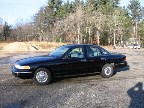 1991 Ford Crown Victoria LTD - A black sedan is parked on a gravel lot with trees in the background.
