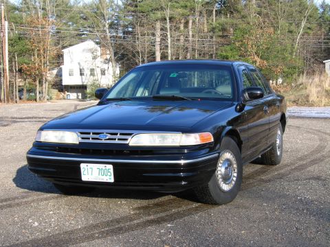 1991 Ford Crown Victoria LTD - A black 1991 Ford Crown Victoria is parked on a gravel lot with a house and trees in the background.
