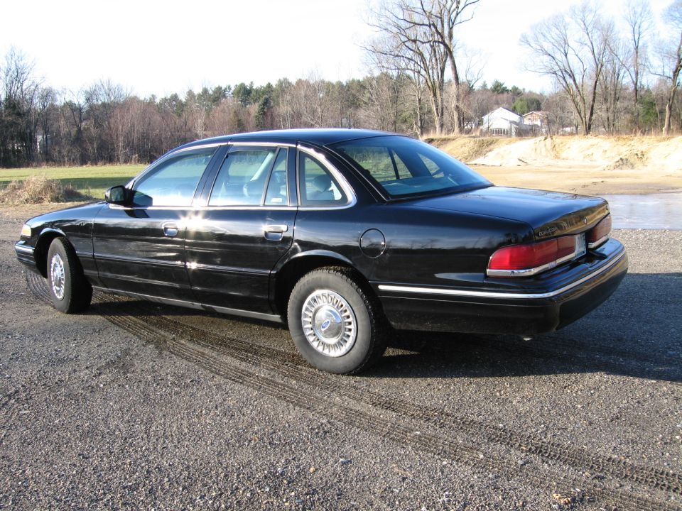 Black sedan parked on gravel, showing its side and rear
