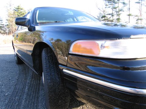 1991 Ford LTD Crown Victoria - A black sedan is viewed from a low angle, highlighting its front corner and chrome accents.