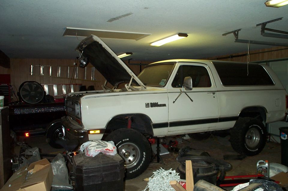 White Dodge Ramcharger SUV with hood open, lifted suspension, and off-road tires in a garage