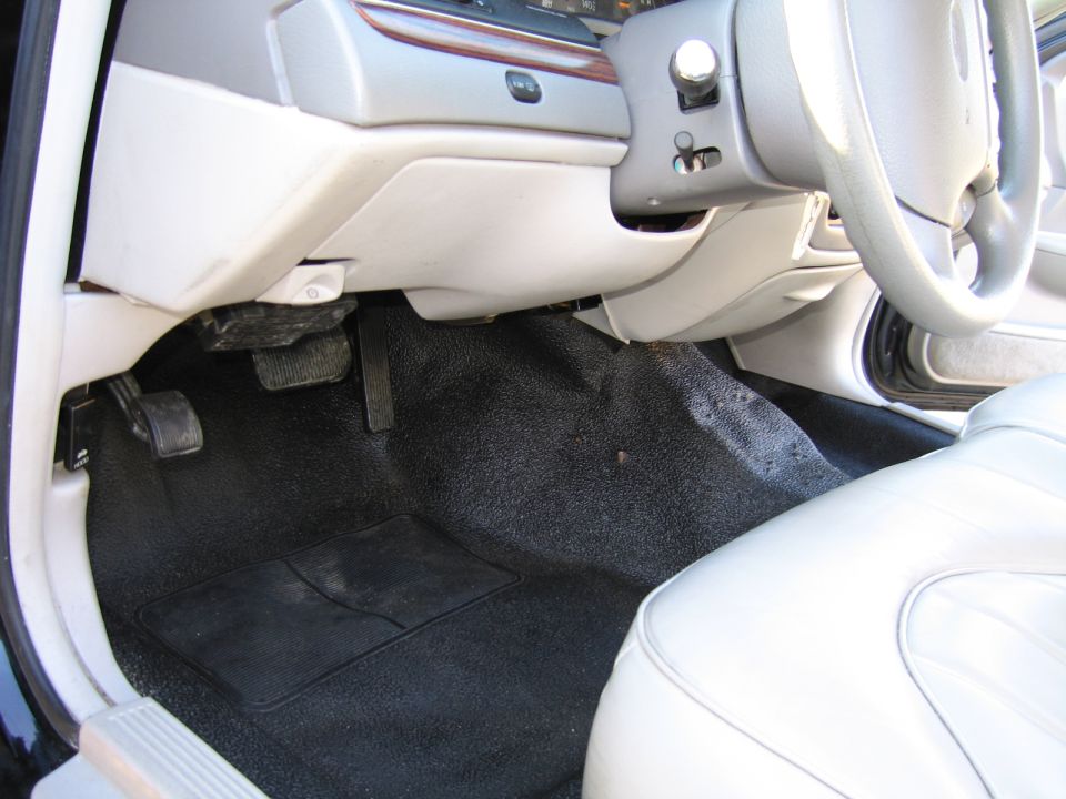 Car interior showing floor pedals, black carpet, and white leather seat