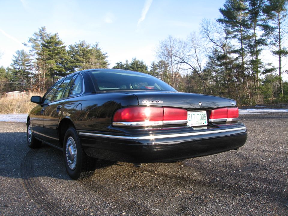 1991 Ford Crown Victoria LTD rear view, parked on gravel with trees in background. License plate reads 217 7005