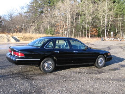 1991 Ford LTD Crown Victoria - This black sedan is parked outdoors on a gravel surface with bare trees in the background.