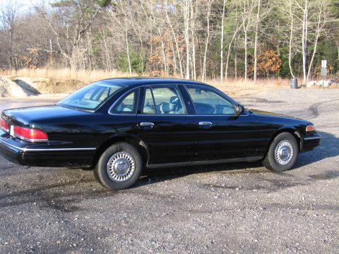 1991 Ford LTD Crown Victoria - A black sedan, likely a 1992 model, is shown from the side on a gravel lot with trees in the background.