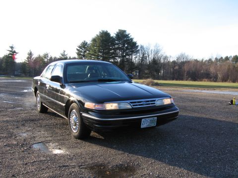1991 Ford LTD Crown Victoria - A black 1991 Ford Crown Victoria is parked on a gravel lot with trees in the background.