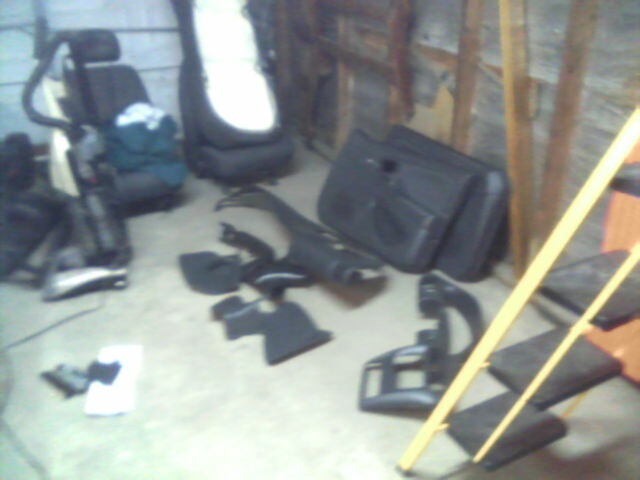Disassembled vehicle interior panels, seats and door card laid out on a garage floor