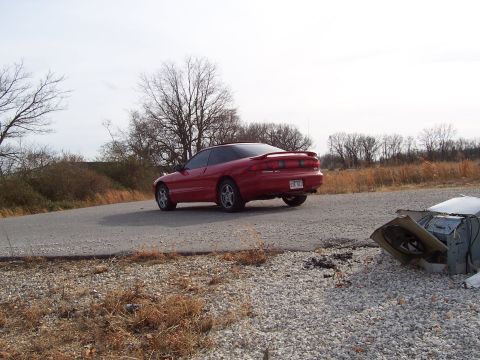 1996 Ford Probe - A red 1996 Ford Probe is seen from the rear on a rural road with debris in the foreground.
