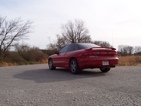 1996 Ford Probe - Rear view of a red 1996 Ford Probe coupe on a gravel road with bare trees in the background.