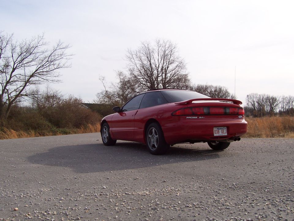Red 1996 Ford Probe coupe parked on a gravel road, rear 3/4 view