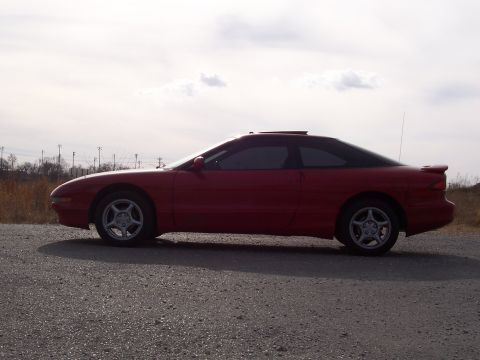 1996 Ford Probe - A red 1996 Ford Probe is parked on a gravel road under a cloudy sky.