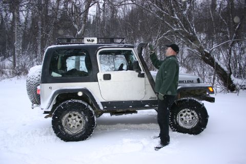 2003 Jeep TJ - A man stands next to a white Jeep Wrangler equipped with a snorkel and roof rack, parked in a snowy, wooded area.