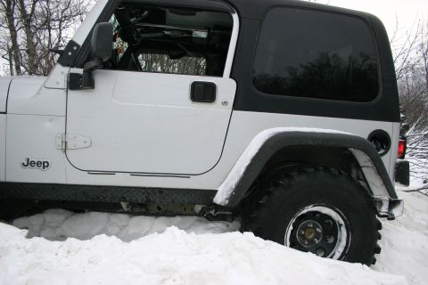 2003 Jeep TJ - A white Jeep Wrangler is partially buried in snow, showing its side profile and large tires.