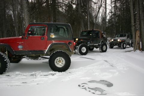 2003 Jeep TJ - Three Jeeps drive through a snowy forest trail during winter.