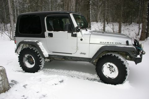 2003 Jeep TJ - A silver Jeep Wrangler Rubicon is parked in a snowy wooded area, with snow covering the ground and the vehicle's tires.