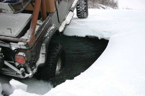 2003 Jeep TJ - A Jeep Wrangler navigates through a partially frozen body of water, with snow covering the surrounding landscape.