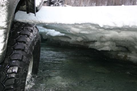 2003 Jeep TJ - A Jeep navigates icy water, its tire splashing as it passes a snow-covered bank.