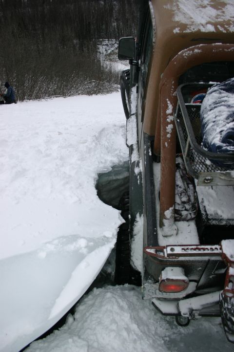 2003 Jeep TJ - A Jeep Wrangler is stuck in a deep snowdrift, with its rear tire partially submerged in a hole.