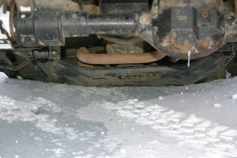 2003 Jeep TJ - The undercarriage of a vehicle is visible, partially covered in snow, with an exhaust pipe and suspension components clearly seen.