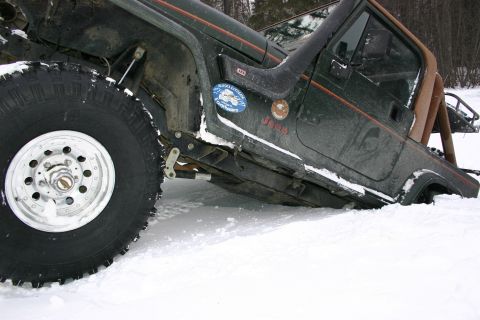 2003 Jeep TJ - A Jeep Wrangler with off-road tires is partially submerged in snow, displaying various decals on its side.