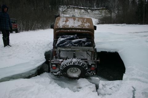 2003 Jeep TJ - A Jeep Wrangler is stuck in a large crack in the ice, with a person observing the situation.