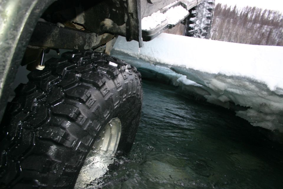 Off-road vehicle tire in icy water, another vehicle visible in background