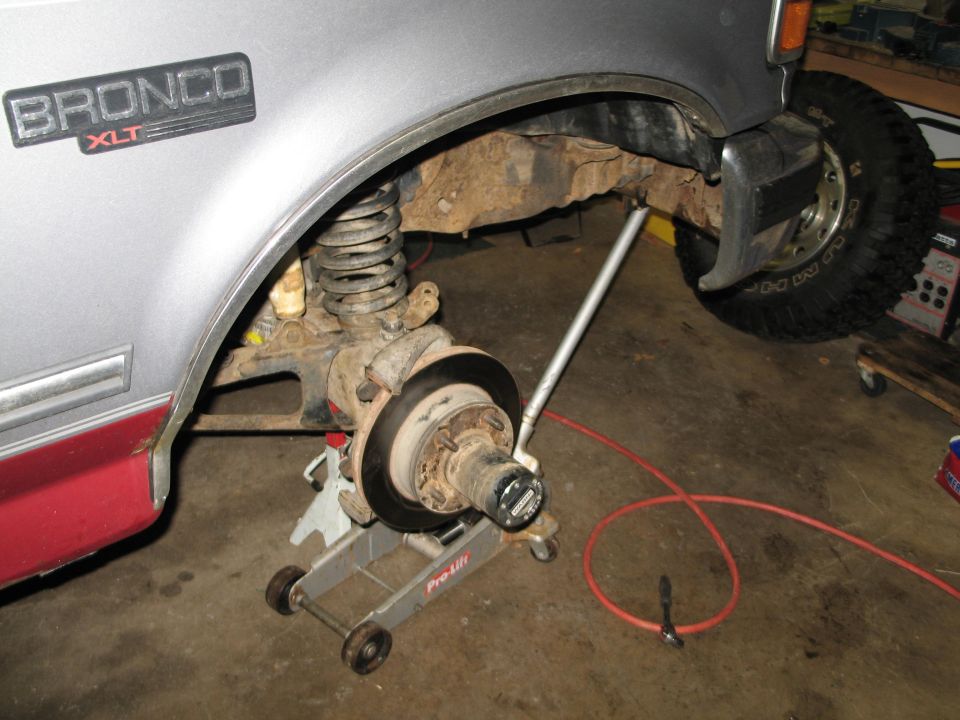 Silver Ford Bronco XLT with red lower trim, front wheel assembly removed and supported by jacks