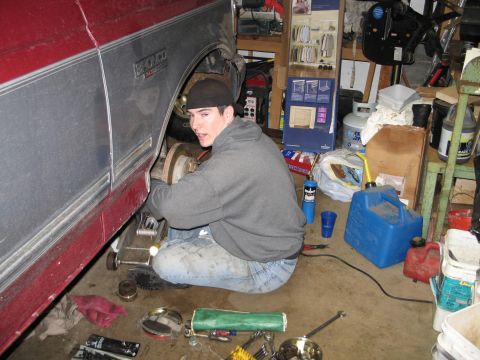 1995 Ford Bronco - A person is working on the brake rotor of a vehicle that is jacked up in a cluttered garage.