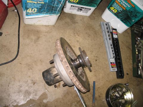 1995 Ford Bronco - A disassembled vehicle wheel hub and brake rotor assembly rests on a garage floor amidst various tools and supplies.