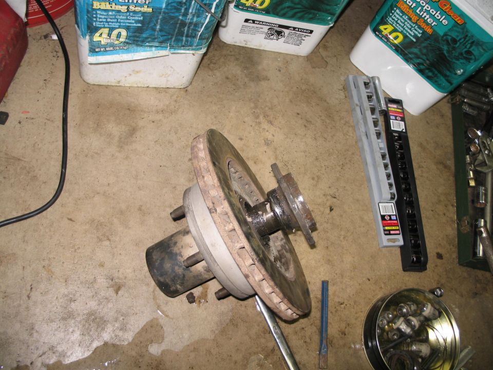 Vehicle wheel hub with brake rotor and studs, lying on a concrete floor next to tool organizers and bags of cat litter