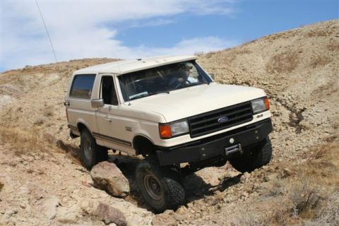 1988 Ford Bronco - White Ford Bronco navigating a rocky off-road trail under a blue sky.