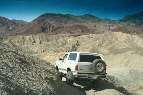 1988 Ford Bronco - A white Ford Bronco navigates a dusty trail through a barren, mountainous desert.
