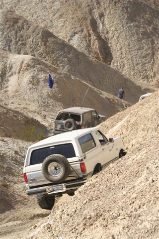 1988 Ford Bronco - A white 1992 Ford Bronco navigates a challenging off-road trail, with another SUV visible further up the incline.