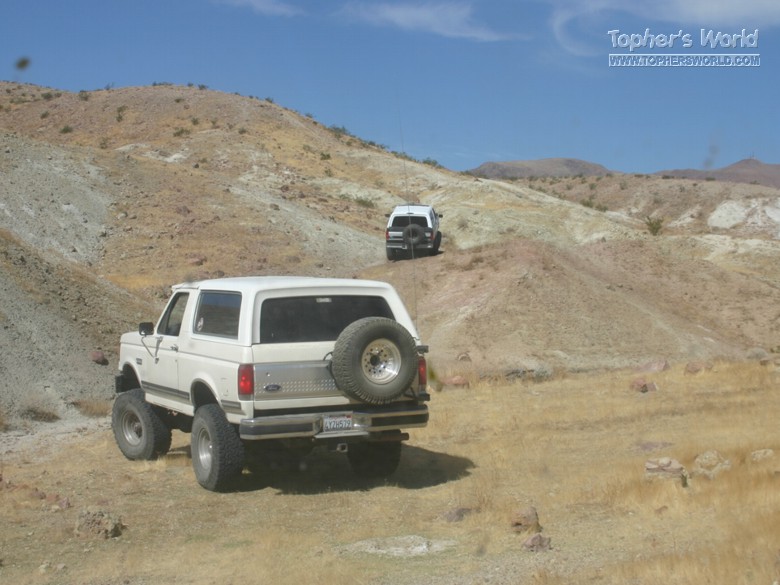 White Ford Bronco and another SUV driving on a dirt road in a desert