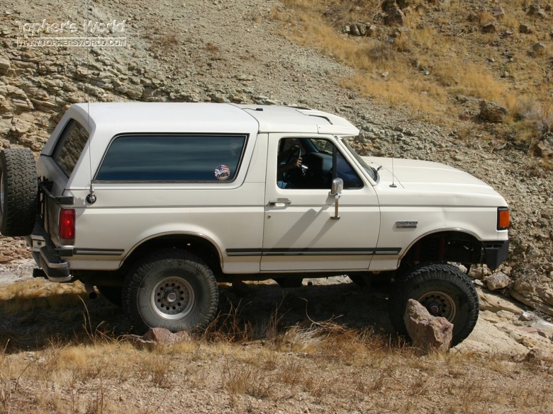 White Ford Bronco on rocky terrain. Spare tire mounted on the back. Lifted suspension