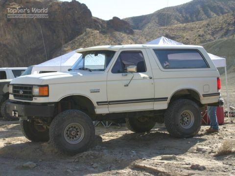 1988 Ford Bronco - A lifted 1987 Ford Bronco is parked in a dusty, outdoor area with tents and mountains in the background.