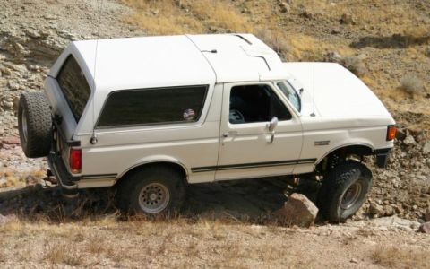 1988 Ford Bronco - This white Ford Bronco, likely from the 1987-1991 generation, navigates a challenging off-road path.