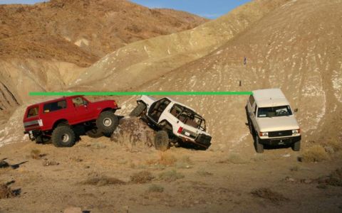 1988 Ford Bronco - Three off-road vehicles navigate a steep, dusty incline in a desert landscape.