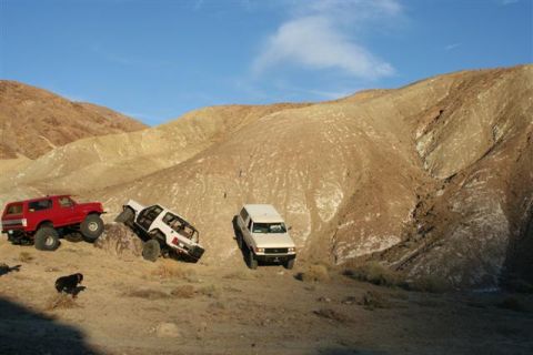 1988 Ford Bronco - Several off-road vehicles navigate a challenging desert landscape with steep, arid hills.