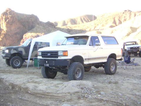 1988 Ford Bronco - A white Ford Bronco is parked in a desert area with other vehicles and a tent.