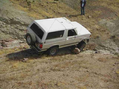 1988 Ford Bronco - White Ford Bronco navigating a rocky, off-road trail with a person observing from a distance.